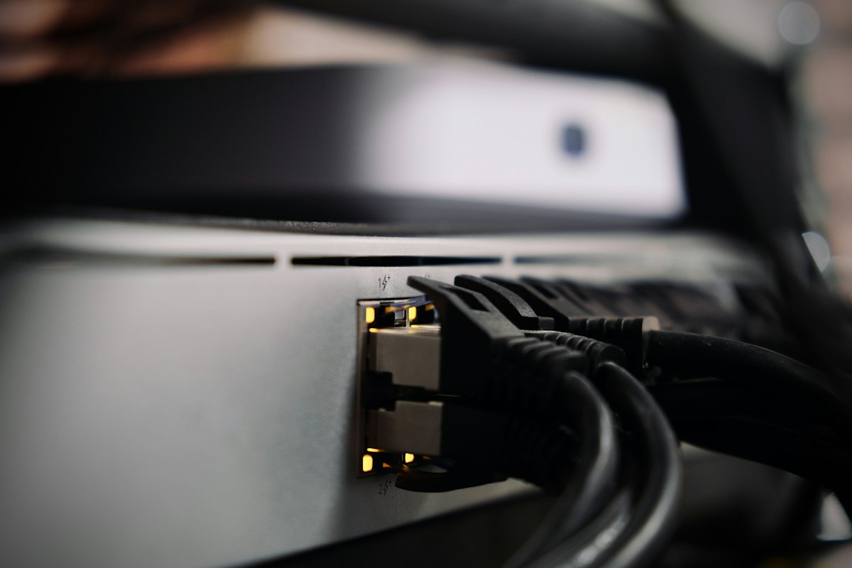 Quelques câbles réseau RJ45 raccordés à un commutateur, dans des tons gris avec des voyants chauds