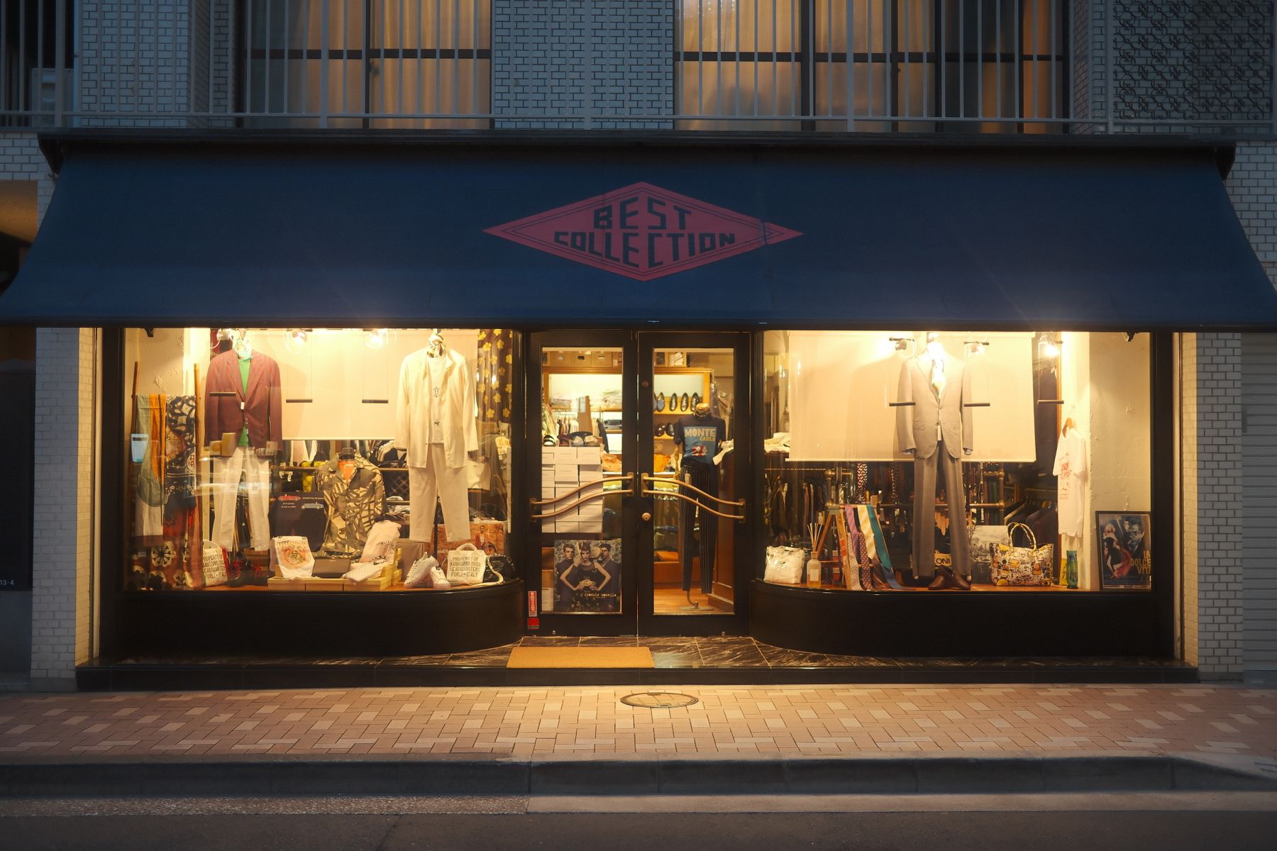 Boutique photographiée de face en soirée, avec entrée centrale et deux vitrines éclairées présentant des vêtements