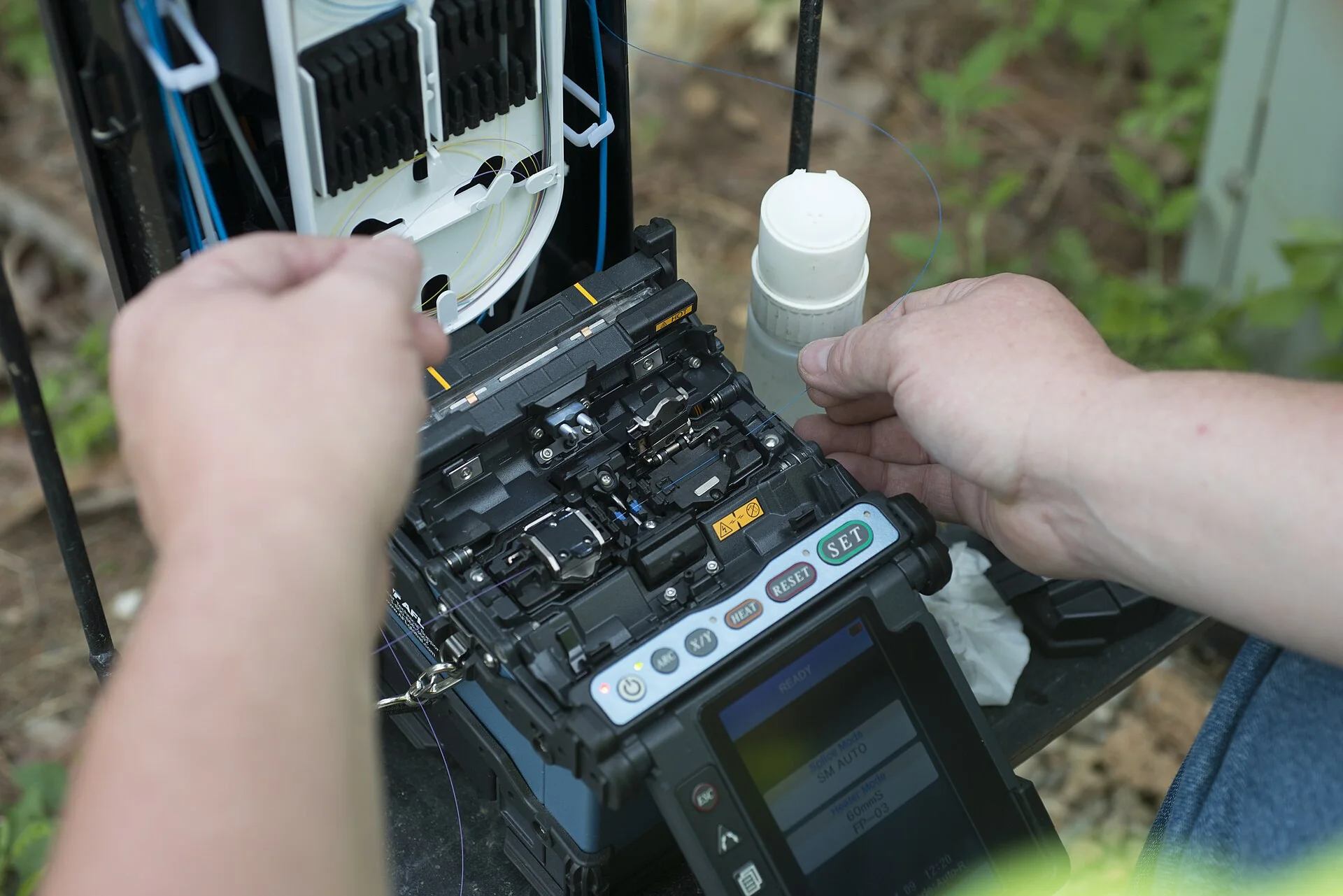 Mains d’un technicien manipulant une fibre près d’un équipement d’épissure